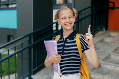 A teenage girl is standing at the stairs with her finger raised up, the girl came up with an idea