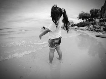 Woman standing on shore at beach against sky