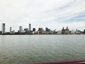 View of buildings by river against cloudy sky