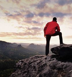 Man in red outdoor jacket on sharp cliff. mountains within early fall daybreak. conceptual scene.