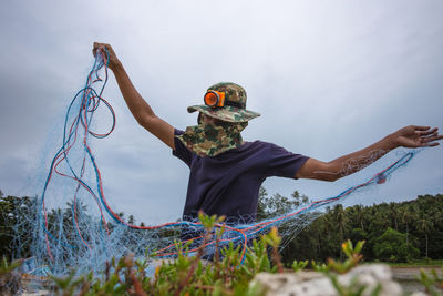 Fisherman holding fishing net on field against sky