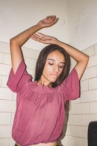 Teenage girl with arms raised while standing against wall