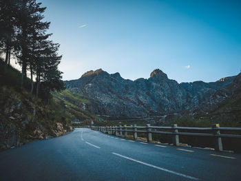 Empty road along trees and mountains against sky