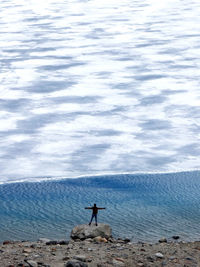 Man standing on rock by sea against sky