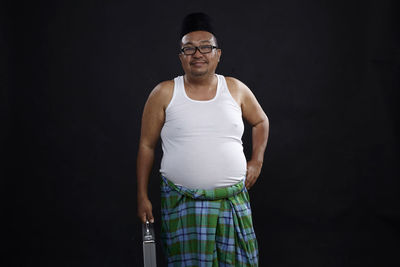 Portrait of smiling mature man with suitcase standing against black background