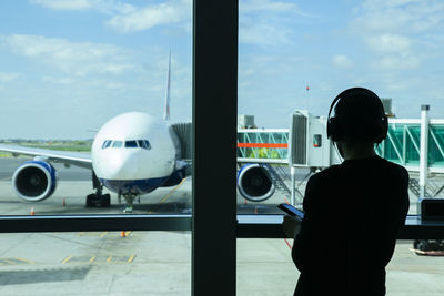 Rear view of man listening music looking through window at airport