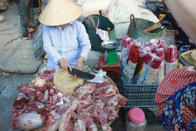 High angle view of butcher wearing asian style conical hat cutting meat at market stall