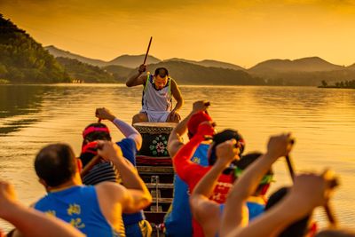 People sitting on boat in lake against sky during sunset