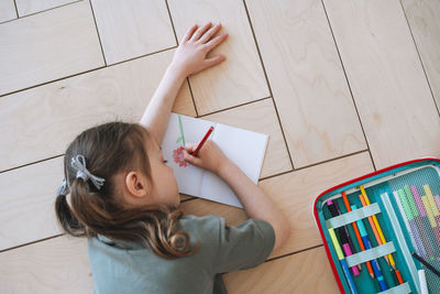 Preschool little girl lying on the floor and drawing at bright room at the home, view from top