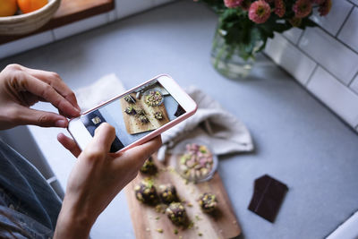 Cropped image of blogger photographing chocolate truffles through smart phone at kitchen counter