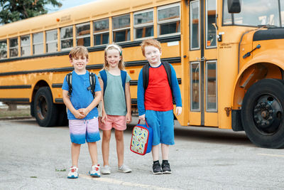 Happy caucasian children boys and girl kids students standing by yellow school bus. education 