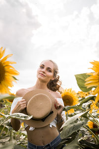 Portrait of young woman standing by flowering plants against sky