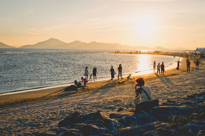 People on beach against sky during sunset