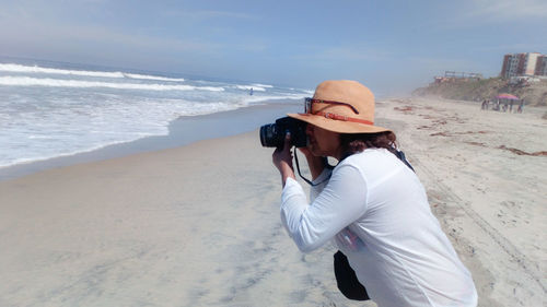 Woman photographing at beach against sky