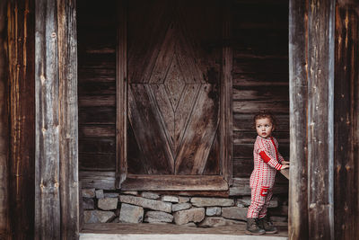 Boy wearing wool onesie in front porch of old wooden house in norway