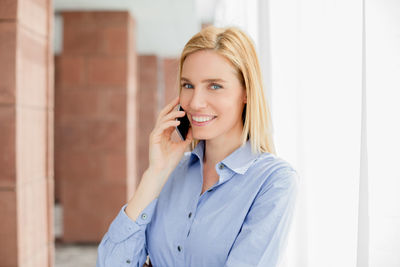 Confident businesswoman talking on smart phone in office lobby