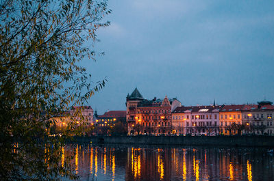 Illuminated buildings by lake against sky at dusk