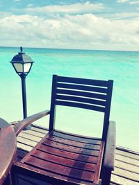 Empty bench by sea against sky