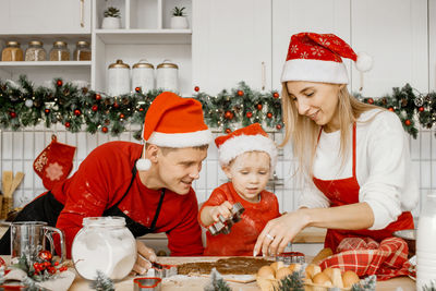 Joyful friendly family wearing christmas hats are cooking gingerbread in the kitchen. 