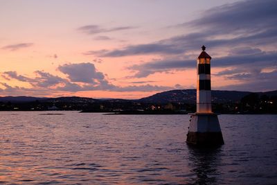 Lighthouse by sea against sky during sunset