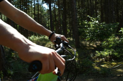 Cropped hands of person holding bicycle handlebar in forest