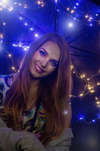 Portrait of smiling beautiful woman against illuminated decoration