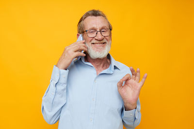 Young man talking on phone against yellow background