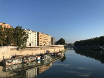 Arch bridge over river by buildings against clear blue sky