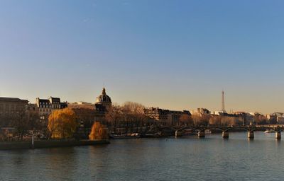 View of buildings by river in city against clear sky