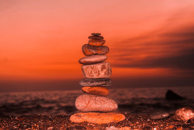 Stack of stones in sea against sky during sunset