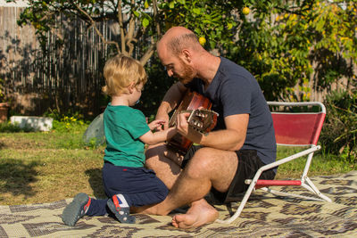 Full length of man teaching guitar to son in backyard