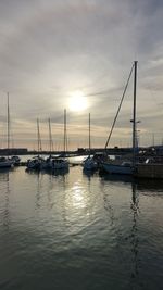 Sailboats moored in harbor at sunset