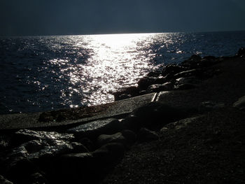 Close-up of hand by sea against sky during sunset