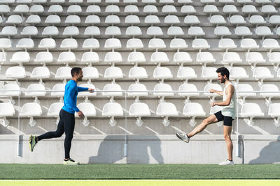 Full length of men exercising against chairs in stadium