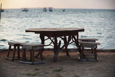 Empty chairs and table by sea against sky