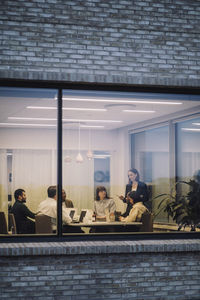 Businesswoman discussing with male and female colleagues seen through window of office