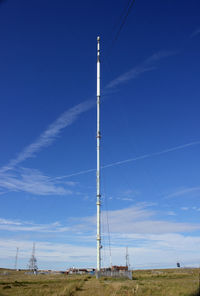 Low angle view of electricity pylon on field against blue sky