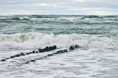 Scenic view of blue sea with foaming waves. vintage long wooden breakwaters stretching to sea