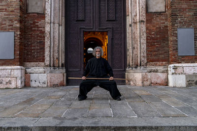 Middle aged tai chi master showing stick exercises outdoors amidst of a medieval cathedral