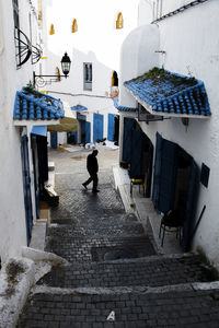 Rear view of man walking on street amidst buildings