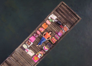 High angle view of woman lying on wooden pier amidst purses over lake