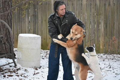 Man with dogs standing on snow against wall