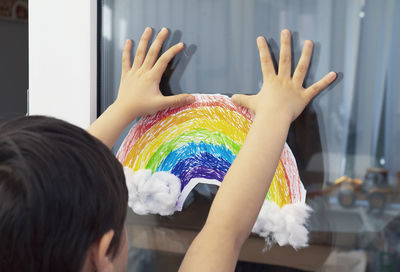 Rear view of boy sticking rainbow drawing on glass