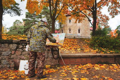 Rear view of man painting on footpath during autumn