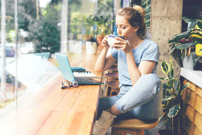 A young girl sits at the tables at the window in a cafe with a laptop.