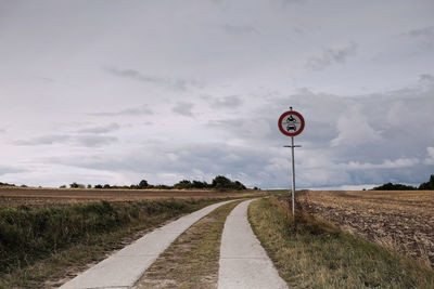Road sign on field against sky