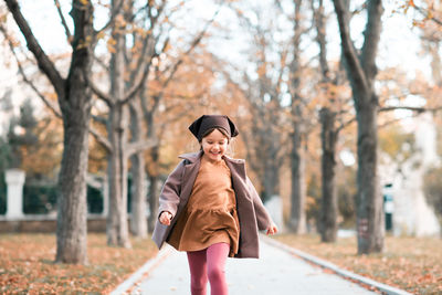 Happy smiling child 4-5 year old wear jacket and hat in park with fall leaves over nature background