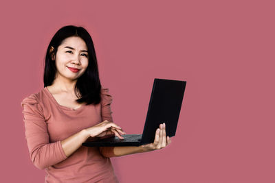Portrait of smiling young woman using smart phone against pink background