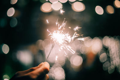 Midsection of person holding firework display at night