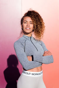 Self confident adult female athlete in sportswear with folded arms looking at camera on two color background with shade